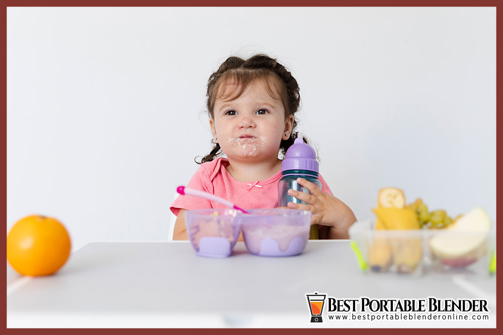 baby-girl-drinking-milk-from-baby-bottle-with-fruit-puree-on-the-table